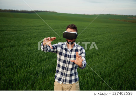 Conception of gaming. In virtual reality glasses. Handsome young man is on agricultural field 127402559
