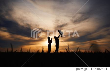 Holding little baby in hands. Silhouettes of father and mother that are outdoors against sunset dramatic sky in the field 127402591