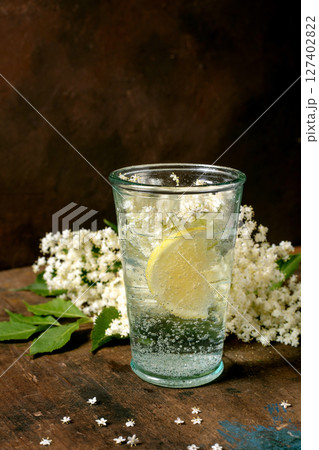 Glass sparkling water with lemon slice elderflower blossoms on rustic wooden table. Natural refreshing drink with white flowers decoration Glass sparkling water with lemon slice elderflower blossoms on rustic wooden table. Natural refreshing drink with white flowers decoration 127402822