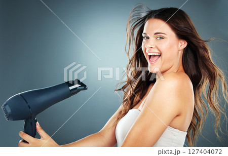 Woman, hair and hair dryer with smile in studio for self care, hair care or cosmetics by blue background. Girl, happy and excited with hairdryer for wellness, cosmetic care and beauty by backdrop 127404072