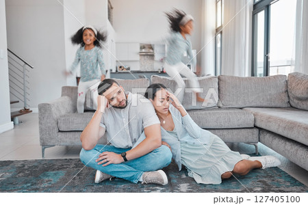 Tired, parents and children jump on sofa with frustrated mom and dad sitting on floor in living room. Family, exhausted couple and playful kids with energy jumping on couch at home during quarantine 127405100