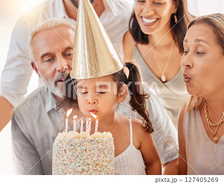 Blowing candles, birthday cake and happy family with a girl to celebrate with a wish, food and eating at a birthday party. Happy birthday, smile and kid with parents and grandparents at a celebration 127405269