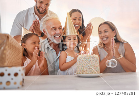 Family, birthday party and cake with celebration, clapping and singing with candle or gift on table in home. Girl, parents and grandparents with sister celebrate event in house with birthday cake 127405281