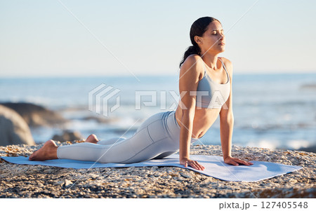 Yoga, fitness and woman at the beach for exercise while in cobra pose for breathing, zen and wellness on rock while on vacation in summer. Female by sea to meditate, workout and practice mindfulness 127405548