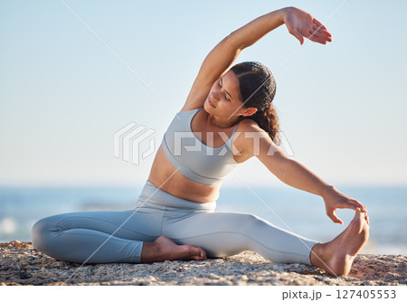 Fitness, exercise and yoga at the beach with a young woman doing spiritual, chakra and zen workout on a rock by the sea. Aesthetic model outdoor for stretching, mindfulness and wellness in nature 127405553