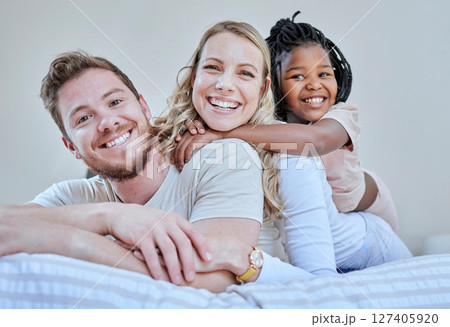 Family, parents and child in interracial portrait on bed with smile, love or happy bonding together in home. Bedroom, multicultural diversity and black girl with foster mom, dad or happy family relax 127405920