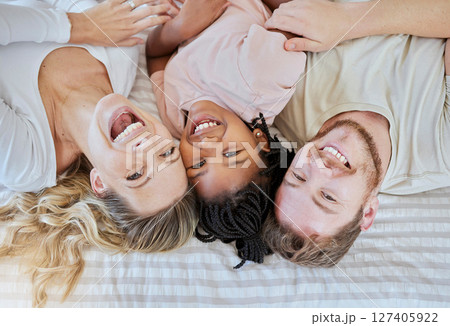 Family, children and adoption with a mother, father and daughter lying on a bed in their home together. Portrait, love and kids with a man, woman and girl bonding in a house bedroom from above 127405922