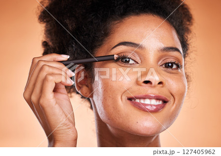 Beauty, skincare and makeup with black woman using eyeliner on eye for facial cosmetics product on a orange studio background. Face portrait of aesthetic model with smile and happiness for self care Beauty, skincare and makeup with black woman using eyeliner on eye for facial cosmetics product on a orange studio background. Face portrait of aesthetic model with smile and happiness for self care 127405962
