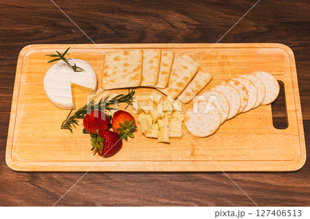Appetizer different types of cheeses on cutting board with fresh strawberries on wooden table. 127406513