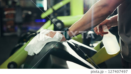 Hands, cleaner and disinfect machine at gym for dirt removal, hygiene maintenance and bacteria protection. Cleaning service, person and sanitizer spray to wipe equipment surface, sanitation or safety 127407497