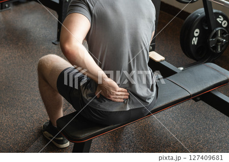 Athlete or young man sitting with pain in lower back at gym with muscle tension. Arm, inflammation or exercise with discomfort at fitness center. Close up. 127409681