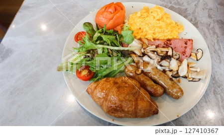 close up of an all day breakfast (English breakfast) with scrambled egg, salad, cherry tomato, smoked salmon, stir fried mushroom, ham, sausage and croissant  127410367