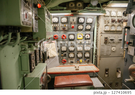 A vintage submarine control bench is surrounded by analog meters, switches, and red valve handles. Panels and gauges are used for monitoring power, pressure, and engine status. 127410695