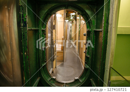 A narrow corridor inside a U.S. Navy submarine is viewed through a green-painted metal hatch. The hallway is lined with doors and bunks, showing the compact layout of the crew area. 127410721