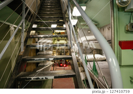 The image shows a narrow metal staircase and sleeping bunks inside a preserved U.S. Navy submarine. The dimly lit corridor reveals compact quarters used by sailors during active missions. The image shows a narrow metal staircase and sleeping bunks inside a preserved U.S. Navy submarine. The dimly lit corridor reveals compact quarters used by sailors during active missions. 127410759
