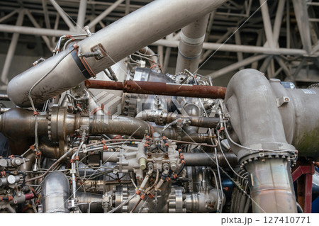 The image shows the upper section of the engine with detailed piping, connections, and oxidizer feed lines. A rusted pipe contrasts with polished stainless steel components. 127410771