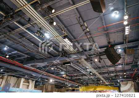 Detailed view of an industrial-style ceiling filled with pipes, lights, and electrical wiring. The infrastructure supports museum or exhibit lighting and air systems. 127410821
