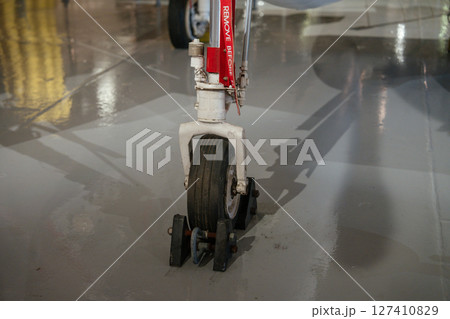 Close-up view of the front landing gear wheel of a military jet secured with chocks. The aircraft is on display in an indoor aviation museum. Close-up view of the front landing gear wheel of a military jet secured with chocks. The aircraft is on display in an indoor aviation museum. 127410829
