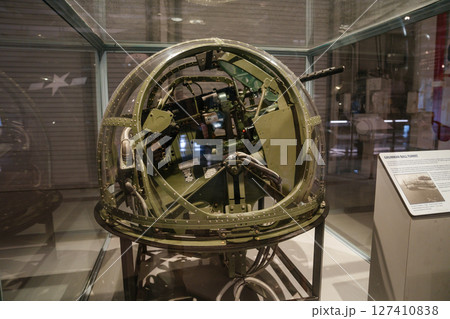 A World War II Grumman ball turret with interior controls and gun is displayed in a museum exhibit. The glass sphere structure is shown behind protective glass with an informational sign nearby. A World War II Grumman ball turret with interior controls and gun is displayed in a museum exhibit. The glass sphere structure is shown behind protective glass with an informational sign nearby. 127410838