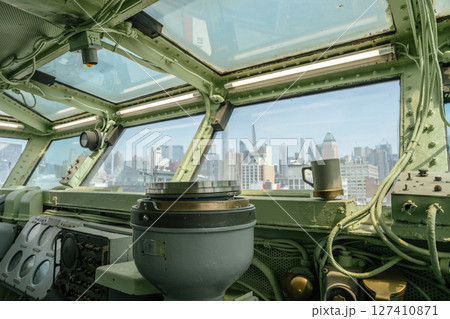 A marine compass is mounted on the control panel inside a ship's bridge. The windows offer a clear view of a modern city skyline with skyscrapers in the background. A marine compass is mounted on the control panel inside a ship's bridge. The windows offer a clear view of a modern city skyline with skyscrapers in the background. 127410871