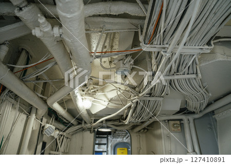 A close-up view of the ceiling in a military ship shows a dense network of pipes and bundled wires. The scene highlights the complex infrastructure and industrial design of naval engineering. 127410891