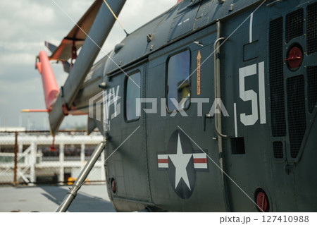 Close-up of a U.S. Navy military helicopter showing the side panel, star insignia, tail rotor, and RESCUE marking. The helicopter is parked on a museum deck under a cloudy sky. 127410988