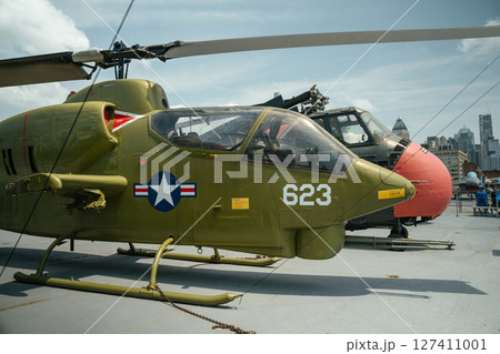 A green U.S. military attack helicopter marked with the number 623 is displayed on the deck of a naval museum ship. The helicopter features rocket launchers and a tandem cockpit under clear skies. A green U.S. military attack helicopter marked with the number 623 is displayed on the deck of a naval museum ship. The helicopter features rocket launchers and a tandem cockpit under clear skies. 127411001