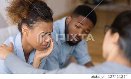 Counselor Comforting Upset African American Wife Crying Next To Husband At Couples Therapy. Selective Focus Counselor Comforting Upset African American Wife Crying Next To Husband At Couples Therapy. Selective Focus 127411234