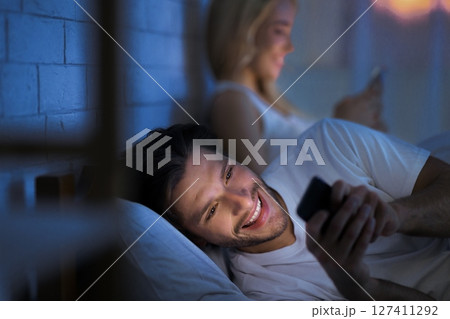 Online Infidelity. Husband Chatting On Smartphone Lying In Bed With Wife At Night. Low Light, Selective Focus Online Infidelity. Husband Chatting On Smartphone Lying In Bed With Wife At Night. Low Light, Selective Focus 127411292