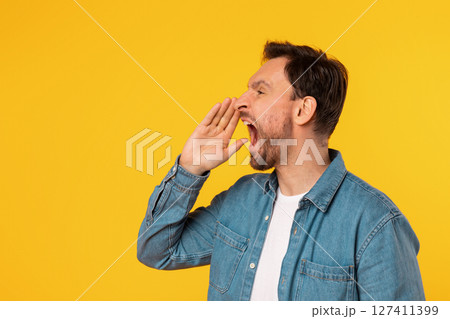 A man with short, dark hair, wearing a light blue button-up shirt, is yelling with his mouth open and a hand cupped near his mouth. He is standing against a plain, bright yellow background. A man with short, dark hair, wearing a light blue button-up shirt, is yelling with his mouth open and a hand cupped near his mouth. He is standing against a plain, bright yellow background. 127411399