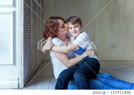Young mother holding her child. Woman and little boy relax in a bright room. Happy family at home. Young mother playing with her son 127411400