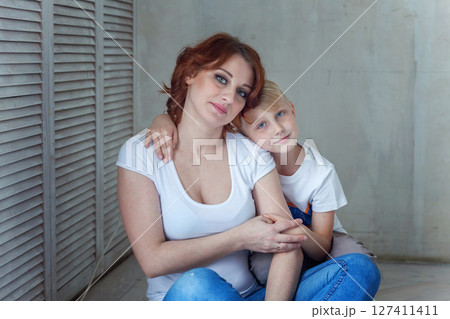 Young mother holding her child. Woman and little boy relax in a bright room. Happy family at home. Young mother playing with her son 127411411
