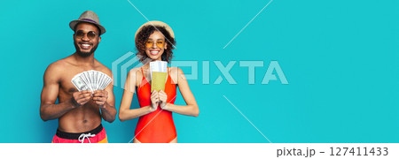 Positive African American lovers wearing swimsuits and sunglasses holding cash and passports, going vacation, isolated on blue studio background, copy space Positive African American lovers wearing swimsuits and sunglasses holding cash and passports, going vacation, isolated on blue studio background, copy space 127411433