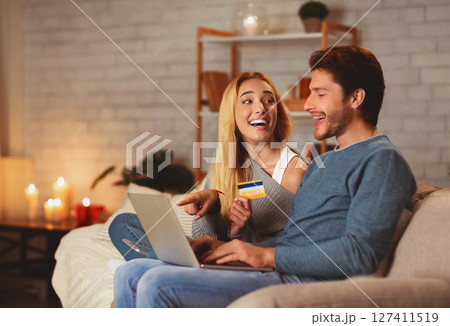 E-Commerce And Online Shopping. Excited Couple Holding Laptop And Credit Card Sitting On Sofa Indoor Buying Things On Internet E-Commerce And Online Shopping. Excited Couple Holding Laptop And Credit Card Sitting On Sofa Indoor Buying Things On Internet 127411519