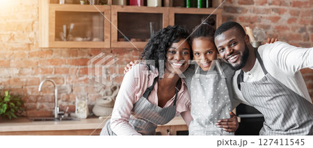 Close african family taking selfie at kitchen, wearing aprons and smiling at camera, copy space 127411545