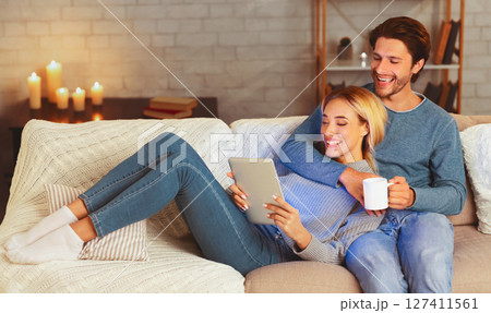 Happy Millennial Couple Using Tablet Computer Watching Movie Relaxing On Couch At Home. Cozy Evening Together 127411561