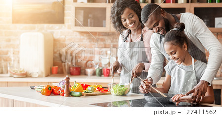 Kind afro parents teaching their adorable daughter how to cook healthy food in kitchen, copy space Kind afro parents teaching their adorable daughter how to cook healthy food in kitchen, copy space 127411562
