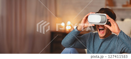 VR. Excited Guy Wearing Virtual Reality Glasses Having Fun At Home In The Evening. Selective Focus VR. Excited Guy Wearing Virtual Reality Glasses Having Fun At Home In The Evening. Selective Focus 127411583