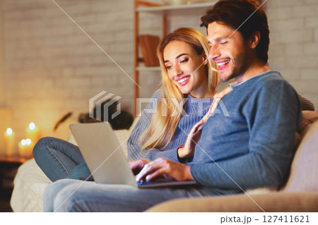 Happy Spouses Browsing On Laptop Sitting Together Relaxing On Sofa At Home. Selective Focus Happy Spouses Browsing On Laptop Sitting Together Relaxing On Sofa At Home. Selective Focus 127411621