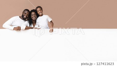 Offer for families. Smiling african american parents and daughter leaning on blank white board with free space for advertisement Offer for families. Smiling african american parents and daughter leaning on blank white board with free space for advertisement 127411623