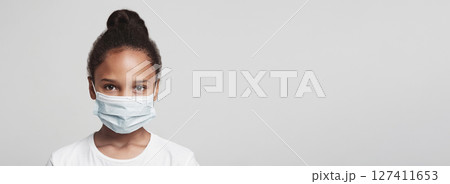 Infection concept. Portrait of little african american girl wearing medical mask, grey background 127411653