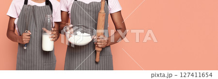 Cropped image of african sisters holding kitchen tools, flour and milk, kids and cooking concept, red background, cropped 127411654