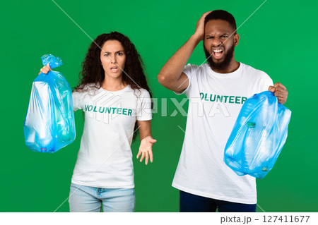 Stop Using Plastic. Two Displeased Multicultural Volunteers Shouting Holding Blue Garbage Bags Full Of Litter Standing On Green Studio Background. Sort Your Waste And Don't Litter Concept 127411677