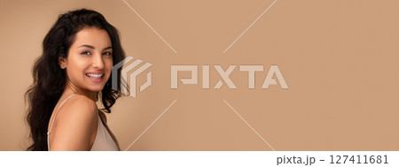 Beautiful brunette long-haired young indian woman posing on beige studio background, smiling at camera, demonstrating silky smooth body skin after SPA treatment, copy space 127411681