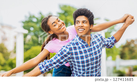A teen black couple is seen laughing and smiling in an outdoor setting. The girl is holding onto guys hand, pulling him playfully towards her. They appear to be carefree and enjoying each other A teen black couple is seen laughing and smiling in an outdoor setting. The girl is holding onto guys hand, pulling him playfully towards her. They appear to be carefree and enjoying each other 127411685
