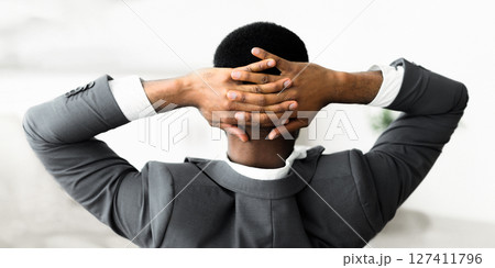 A man in a suit leans back with his arms crossed behind his head. A man in a suit leans back with his arms crossed behind his head. 127411796