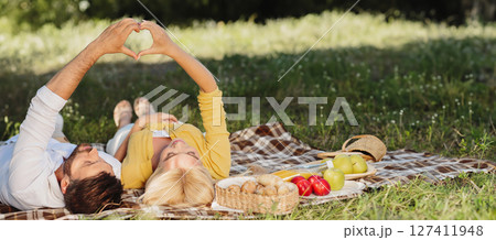 Happy Couple Having Picnic Gesturing Heart Shape Lying On Plaid On Summer Date In Park Enjoying Day Together. Finally, Outdoor. 127411948