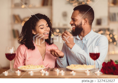 Affectionate young black couple having dinner, guy feeding his girlfriend with pasta. Cute lovers having romantic date, flirting, having fun, celebrating St Valentine's Day or holiday Affectionate young black couple having dinner, guy feeding his girlfriend with pasta. Cute lovers having romantic date, flirting, having fun, celebrating St Valentine's Day or holiday 127412027