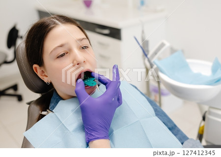 Dentist placing impression tray in girl's mouth for dental care 127412345