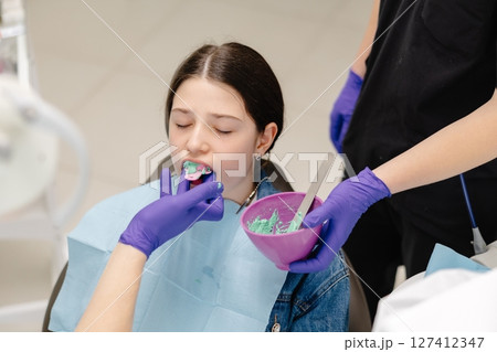 Dentist applying dental mold to young patient's teeth 127412347